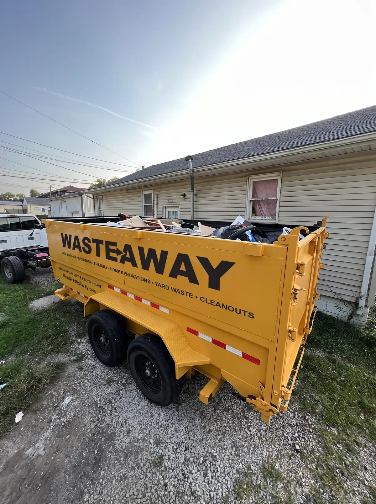 Waste Away dumpster placed on gravel beside a rental house, loaded with cleanout debris